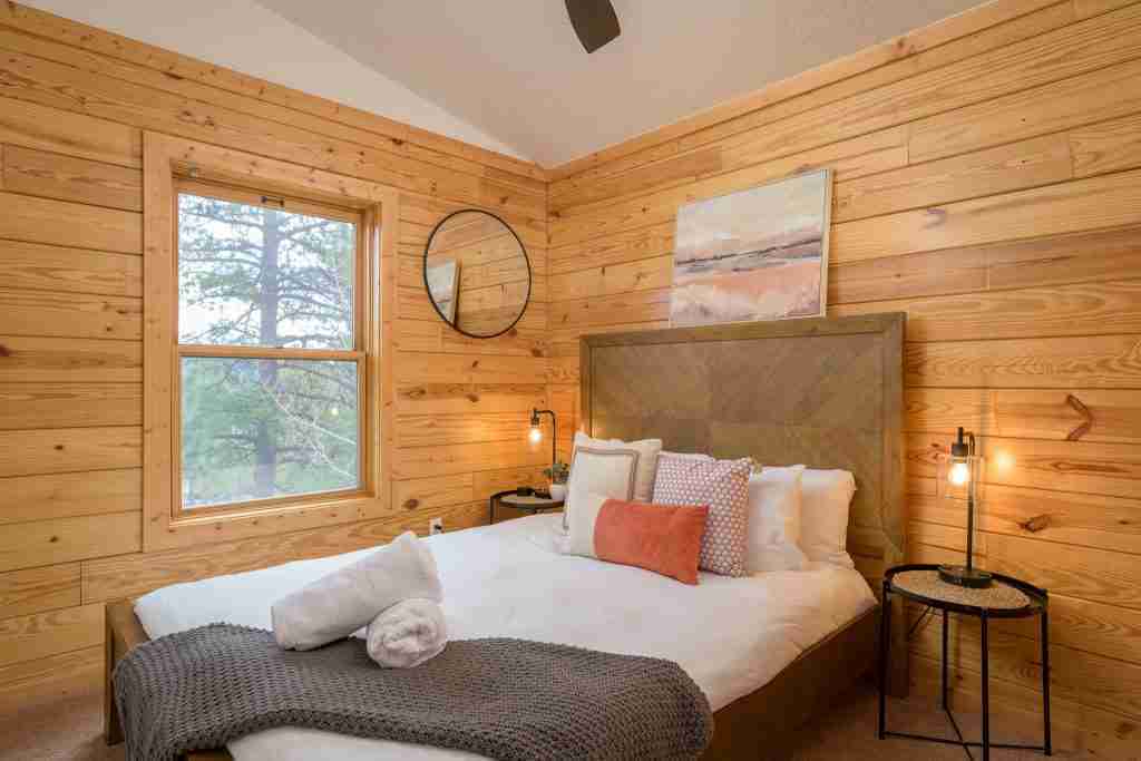 Queen bedroom with knotty pine walls, a round mirror, and bedside lamps