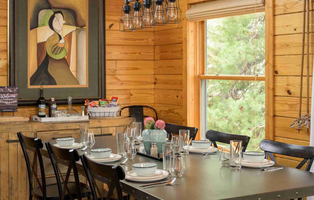 Dining table set for a meal beside a window to the pines