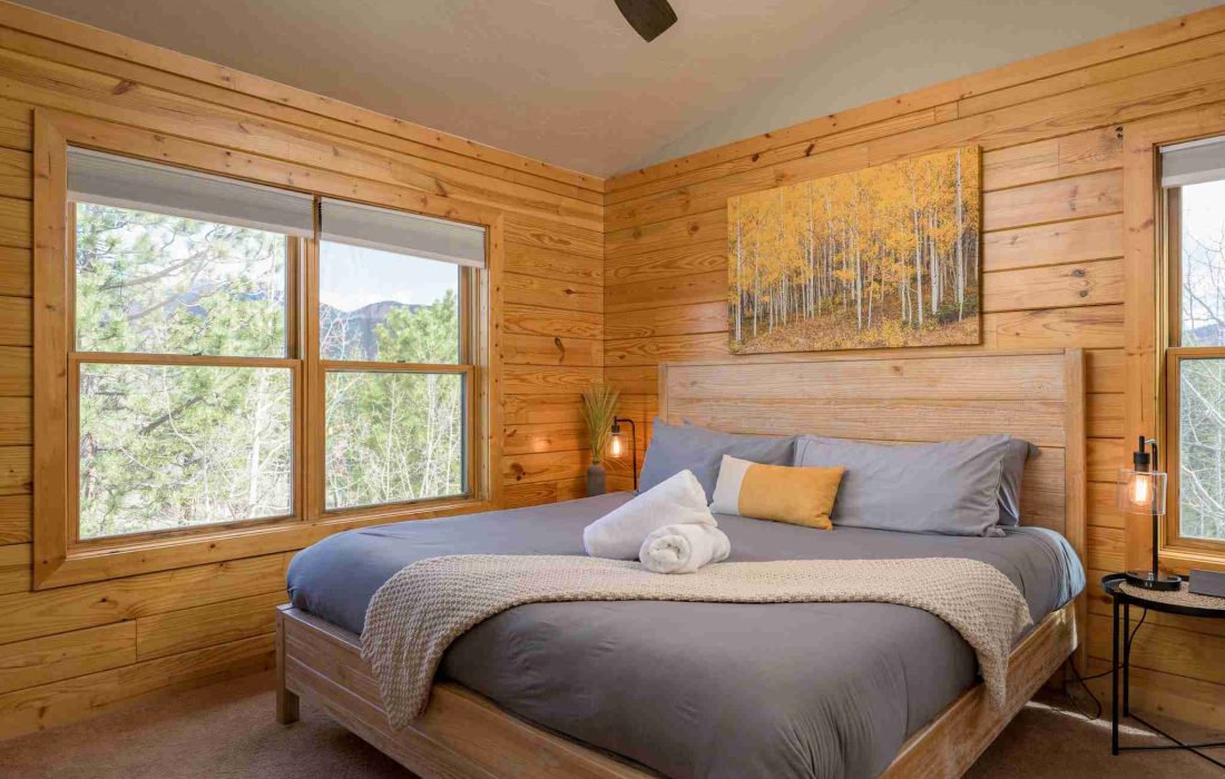 Primary suite with a king bed, aspen art, and windows to the trees