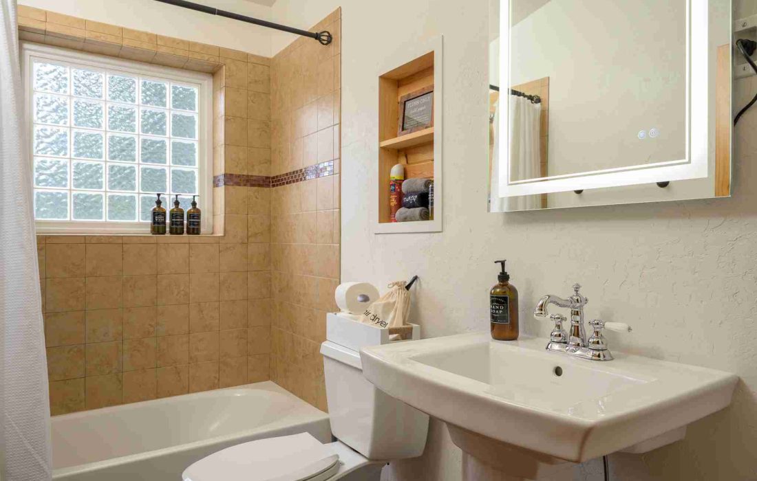 Bathroom with a tub and shower combo, pedestal sink, and lighted mirror