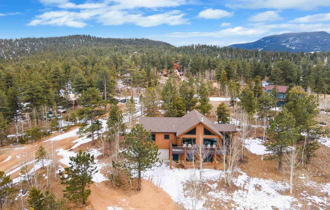 Aerial view of the cabin among the pines, with mountains in the distance